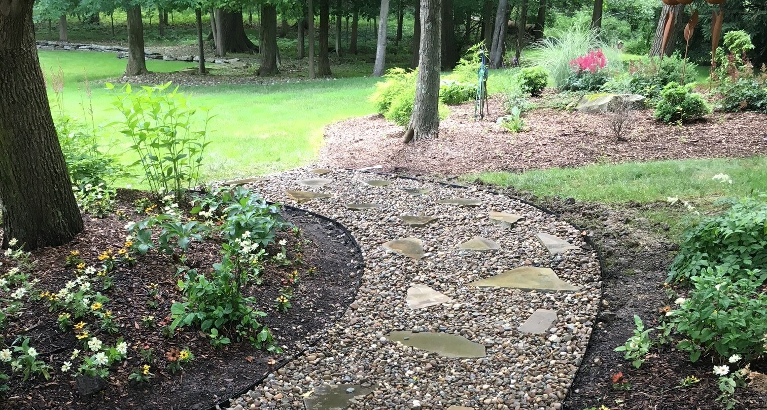 Curving stone garden path through mulch beds and trees in a green yard