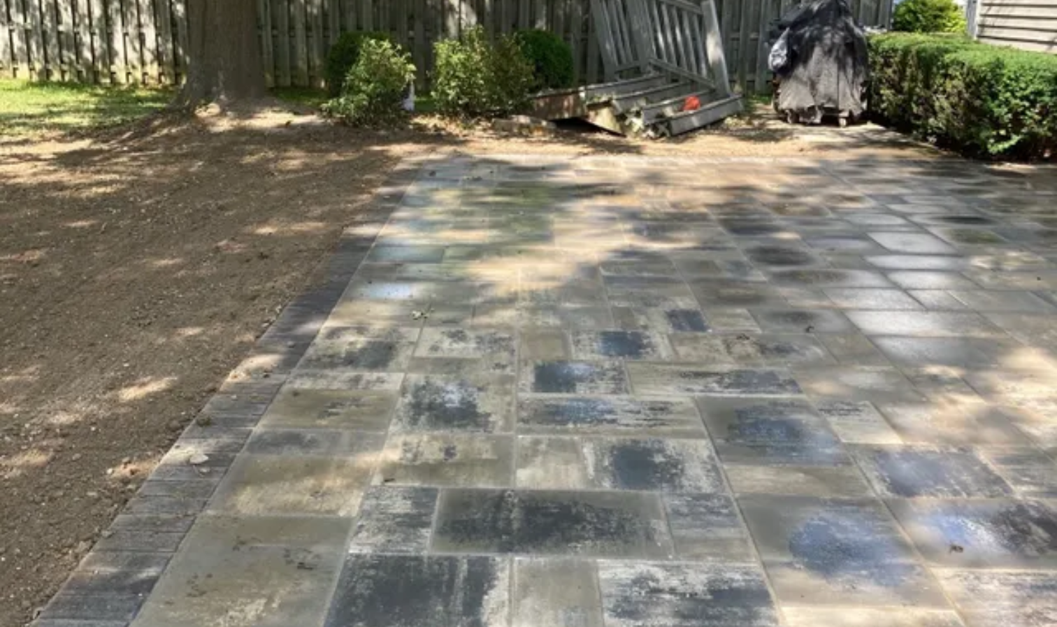 Stone patio with large square pavers beside a dirt yard and wooden fence in daylight