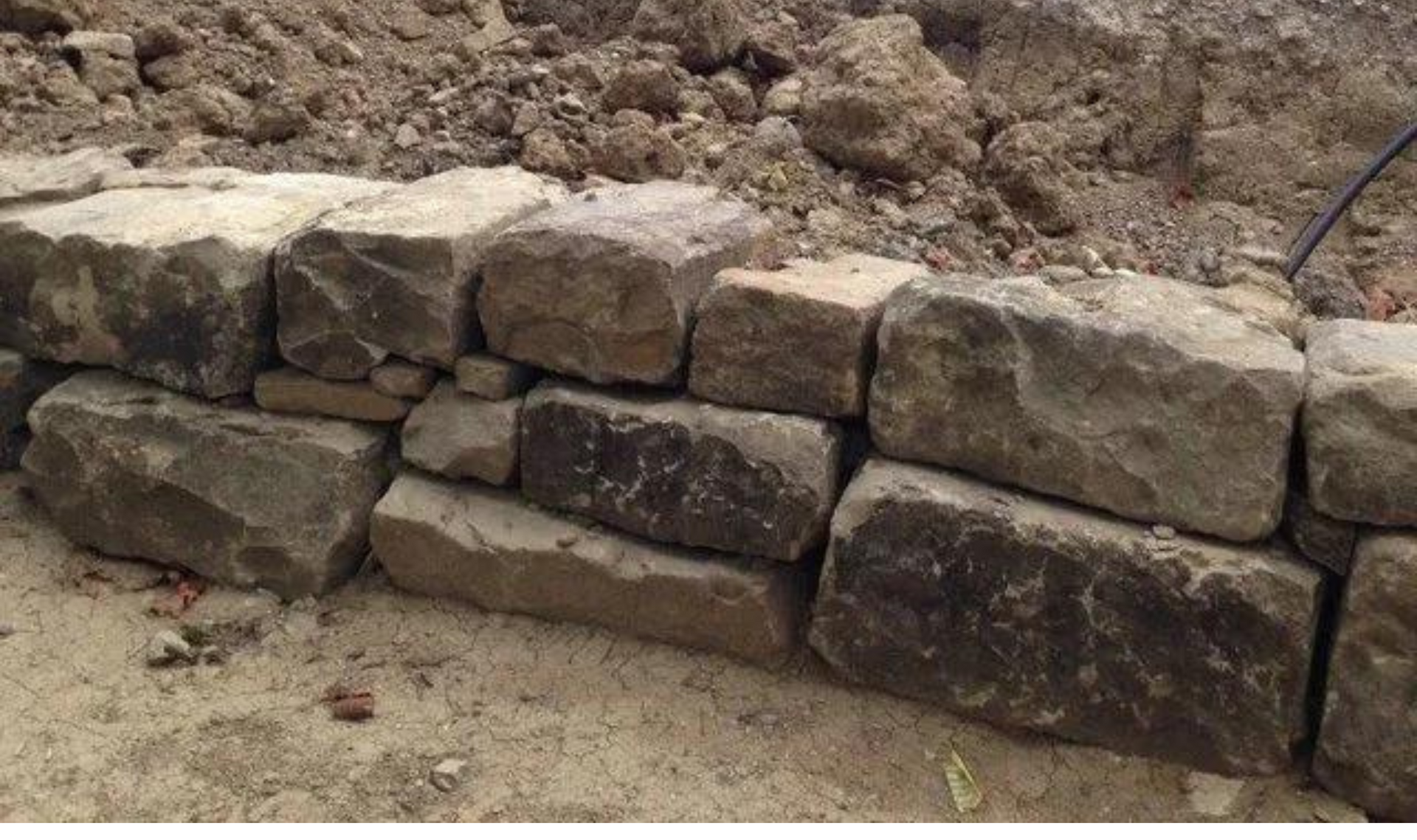 Stacked stone retaining wall along a dirt slope, with rough-cut blocks and exposed earth behind it.