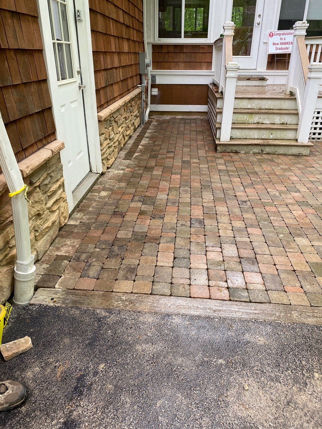 Brick walkway leading to front steps beside a house, with a white railing and downspout.