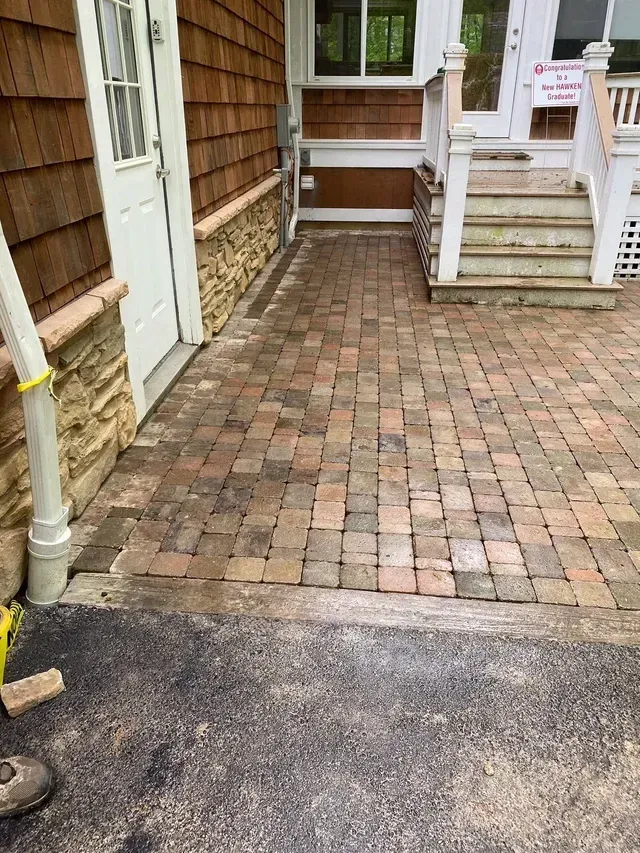 Brick-paved walkway leading to a house entrance with steps and white railings