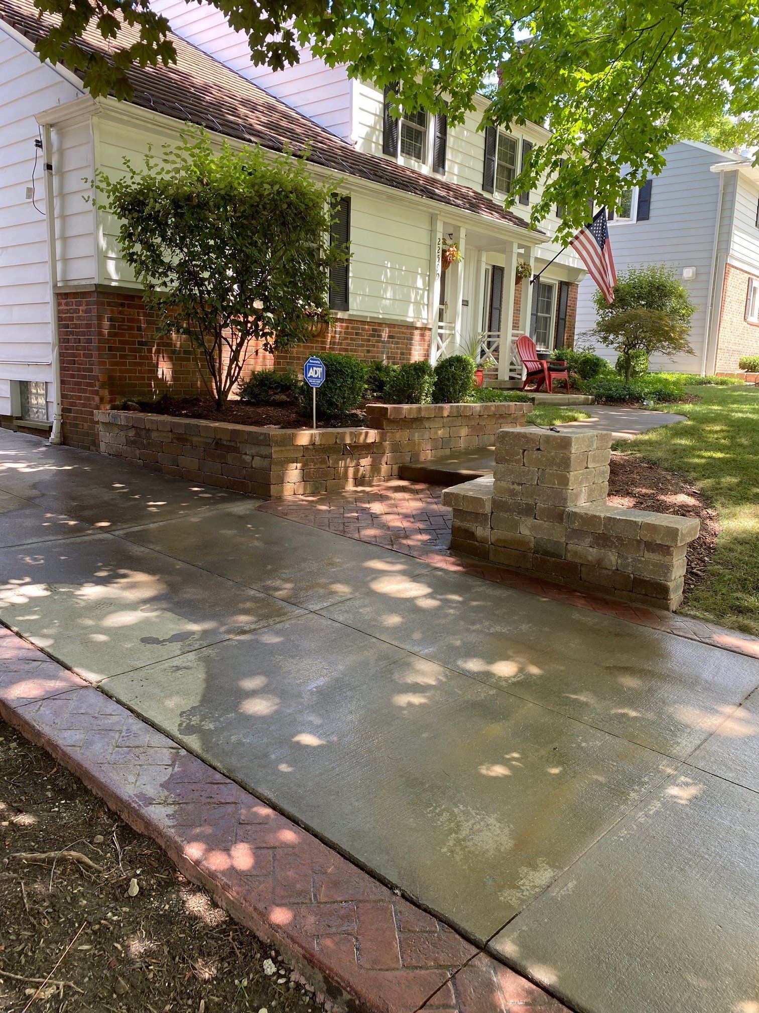 Front walkway beside a white house, with brick steps, a small porch, and sunlit trees overhead