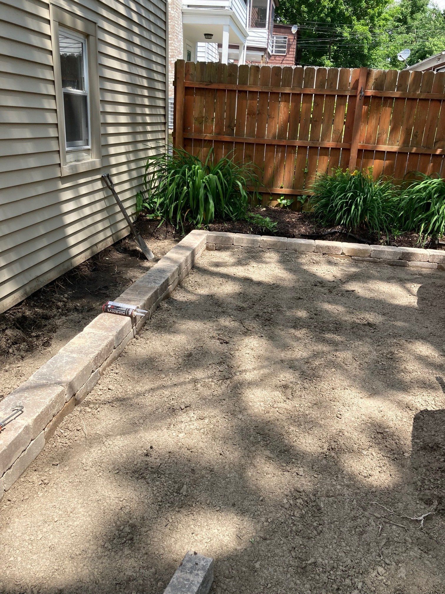 Gravel driveway beside a house, bordered by stone edging, wooden fence, and green plants.