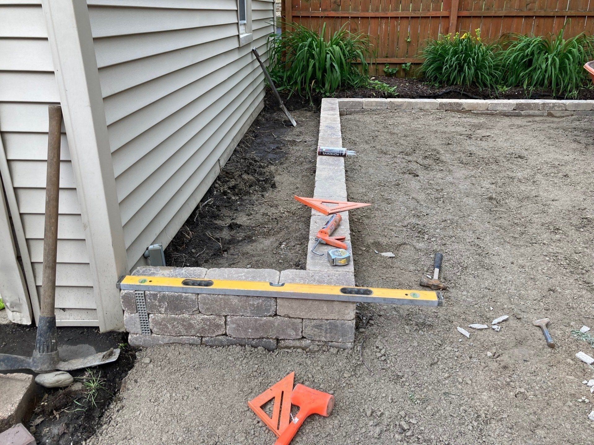 Backyard construction site with concrete block wall, dirt, and orange survey stakes beside house siding