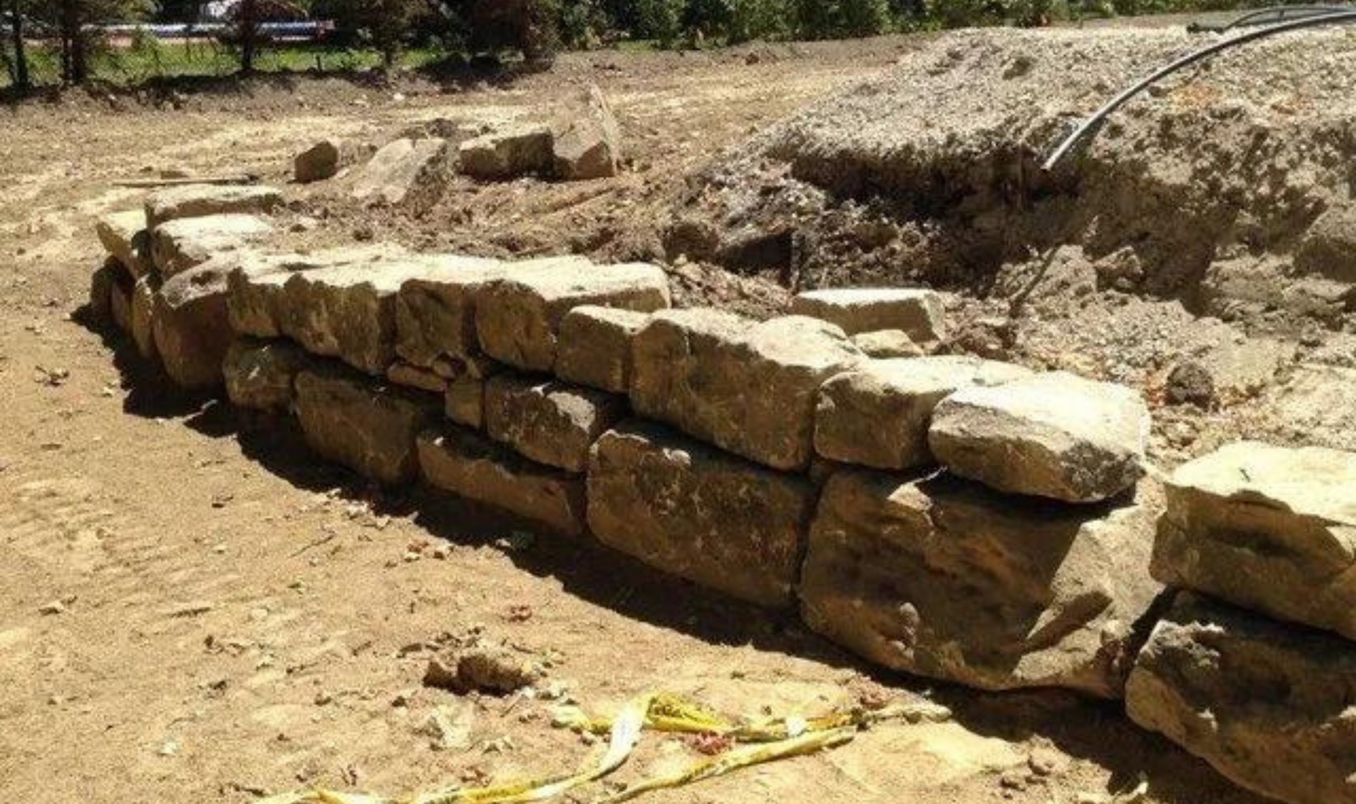 Stone retaining wall under construction on a dirt site outdoors