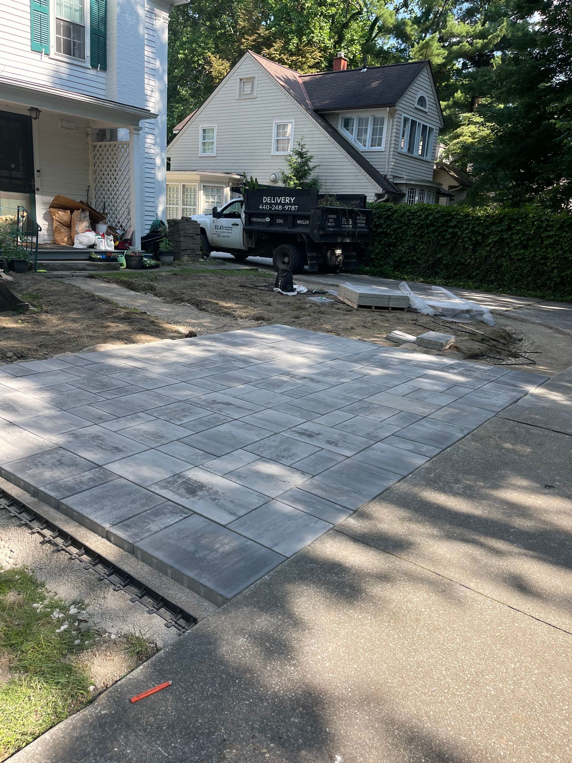 Paved driveway with a pickup truck parked beside a house and a hedge-lined yard