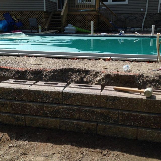 Broken brick pool wall beside a swimming pool, with debris scattered on the ledge.