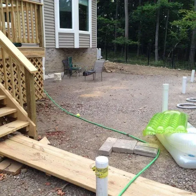 Backyard with a wooden ramp, gravel patio, hose, and chairs beside a house