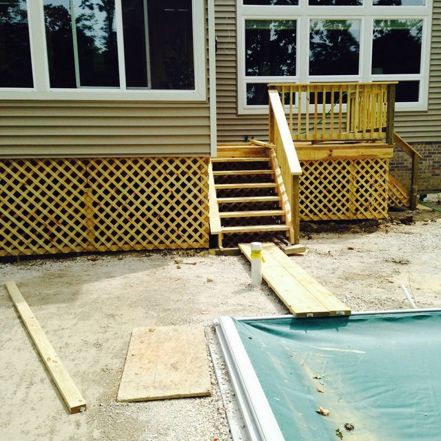 Back porch with wooden steps, ramp, and lattice skirting beside a house under construction