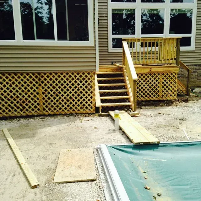 Backyard deck with stairs and ramp, beige siding, and a pool edge in the foreground