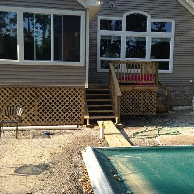 Backyard deck with stairs, lattice skirting, and a pool beside a house