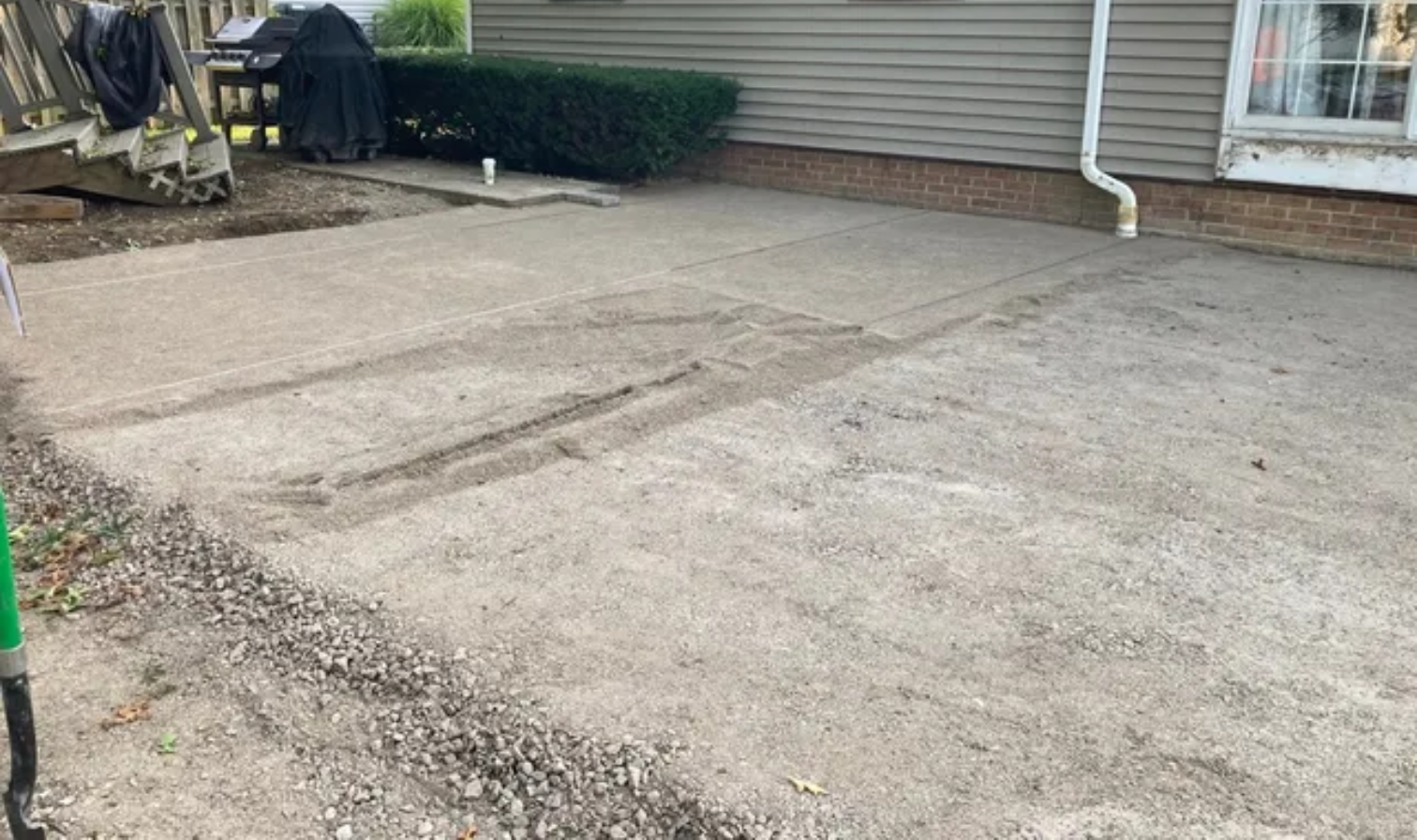 Cracked concrete driveway beside a house with tan siding and a downspout.