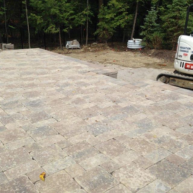 Stone-paved driveway beside a wooded area, with a white van parked on the right.