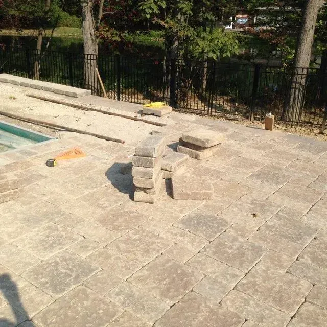 Stone patio with a small curved stacked-stone structure beside a pool and trees in the background