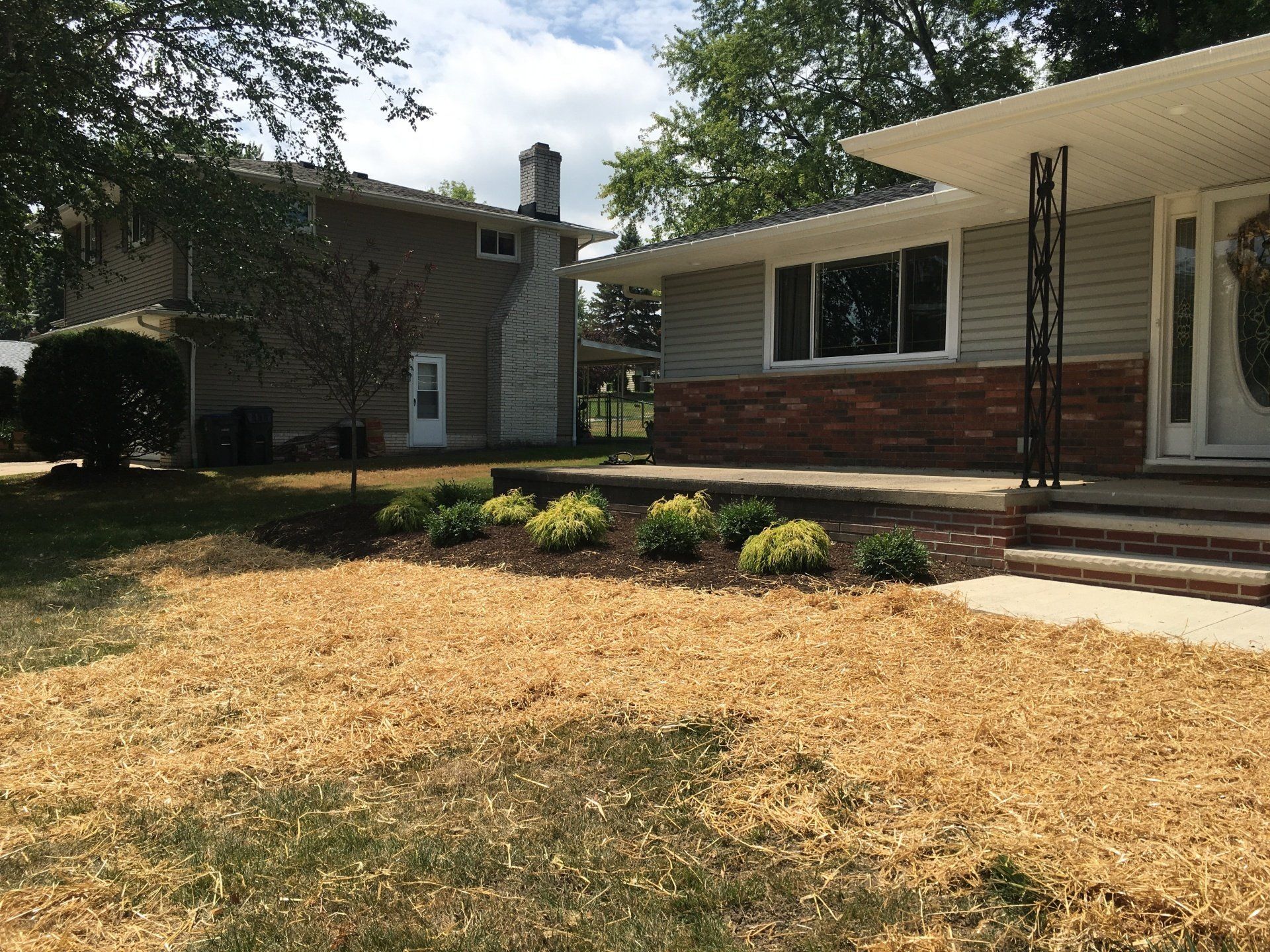 Suburban house with brick and stone facade, front steps, and a dry front lawn under trees