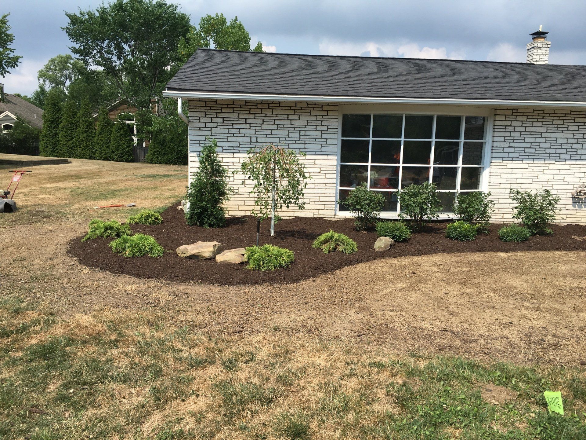 Single-story white house with a large window and fresh mulch landscaping in the front yard.