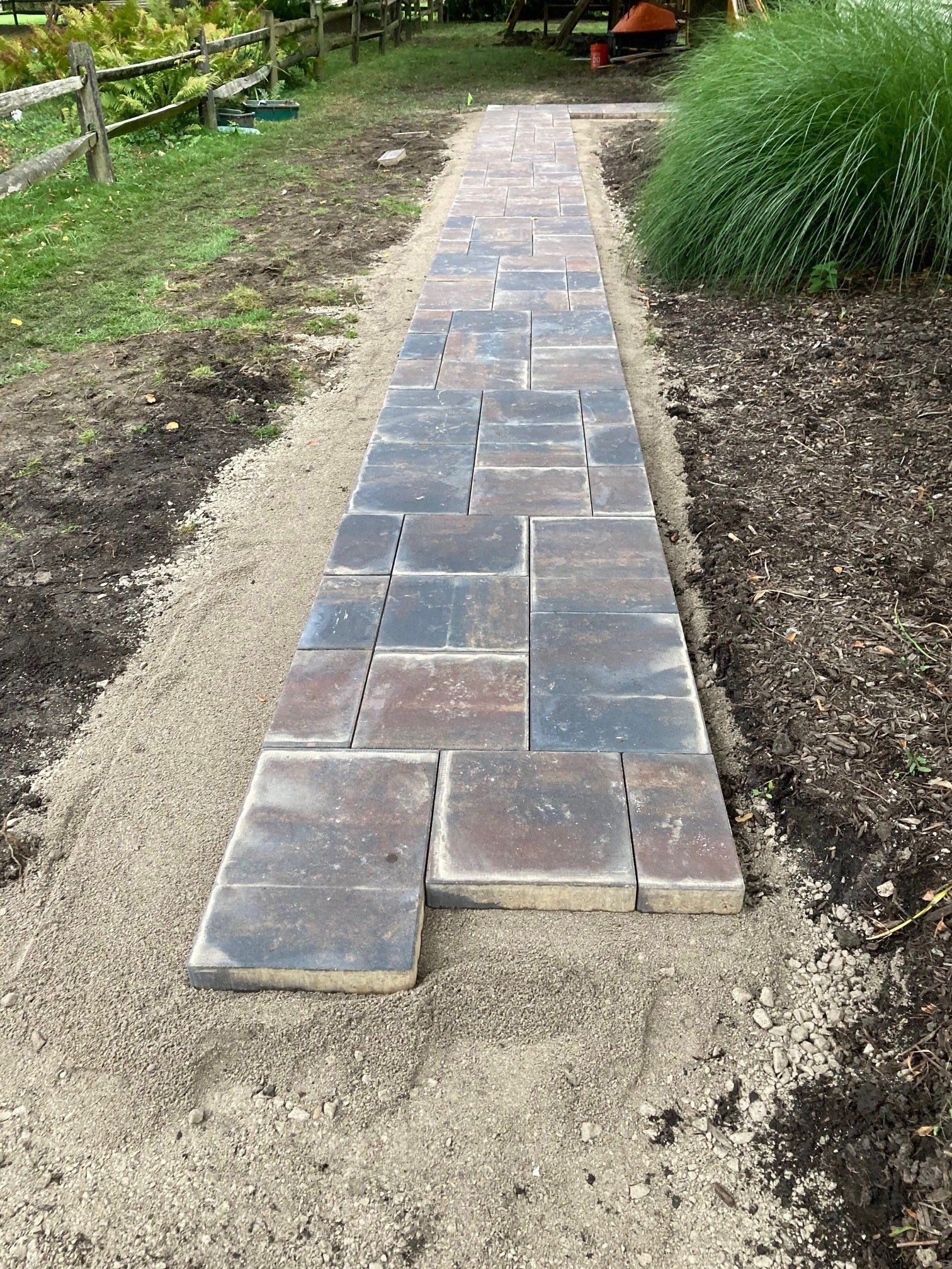 Stone path under construction in a garden, with uneven pavers and bare soil on both sides.