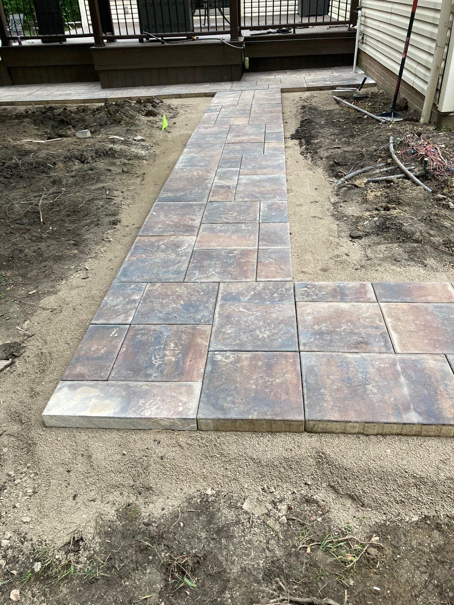 Newly laid stone paver walkway leading to a porch, bordered by bare dirt and shrubs