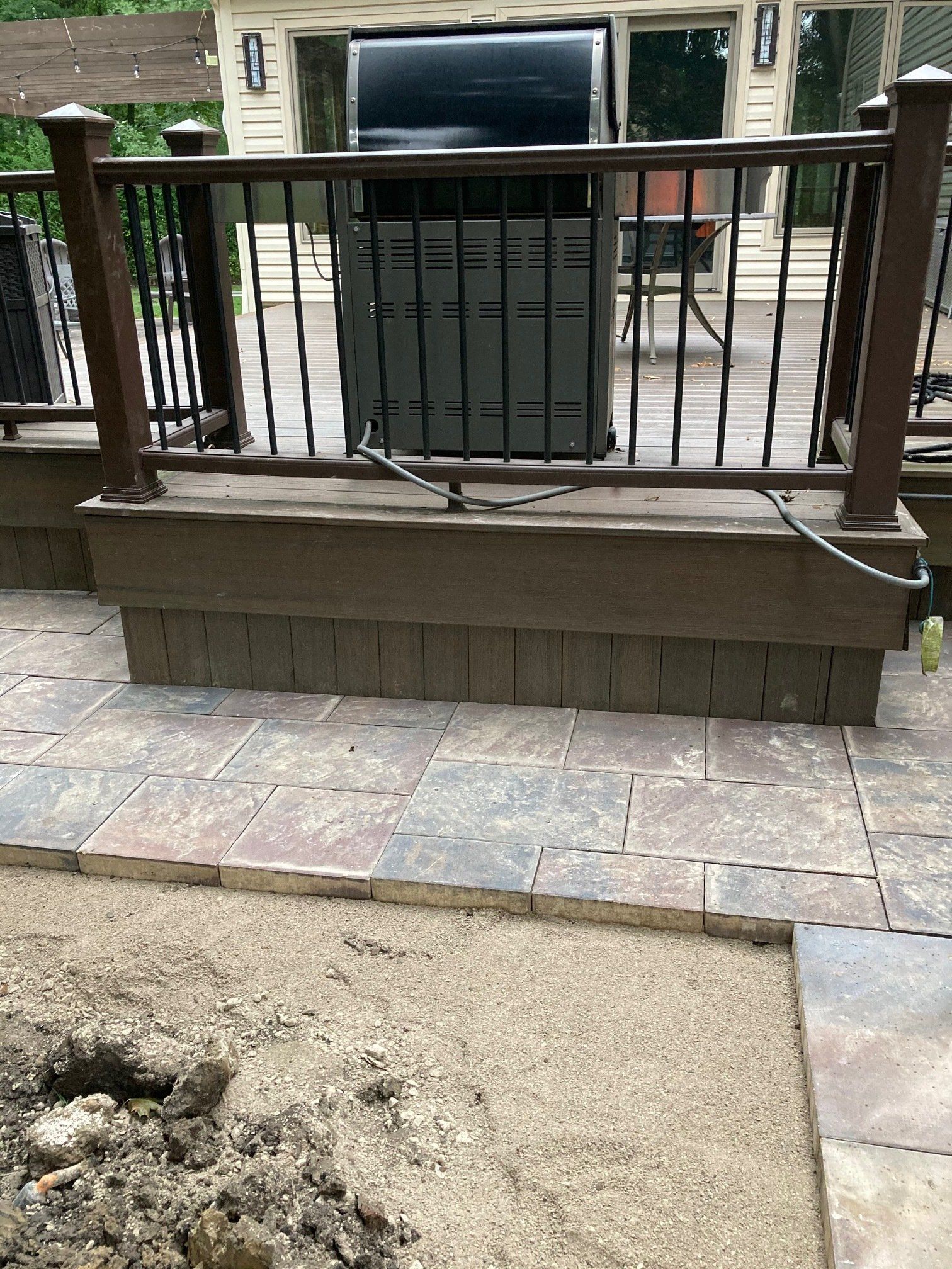 Wooden bench in front of a railing on a stone patio with a sandy area in the foreground