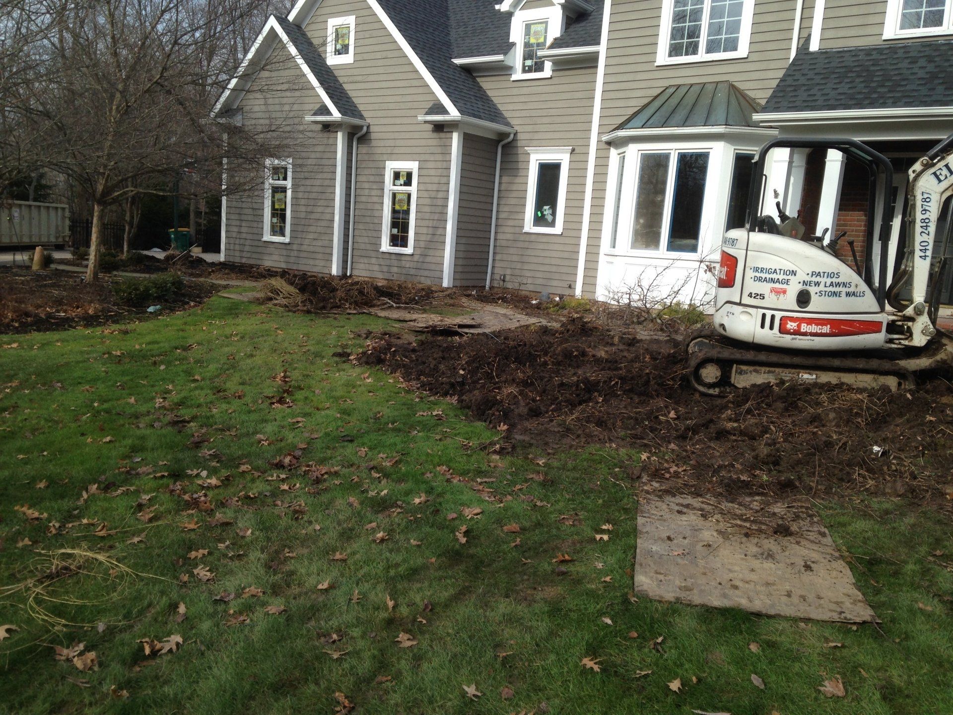 House exterior with a white Bobcat excavator in a muddy yard near the front porch