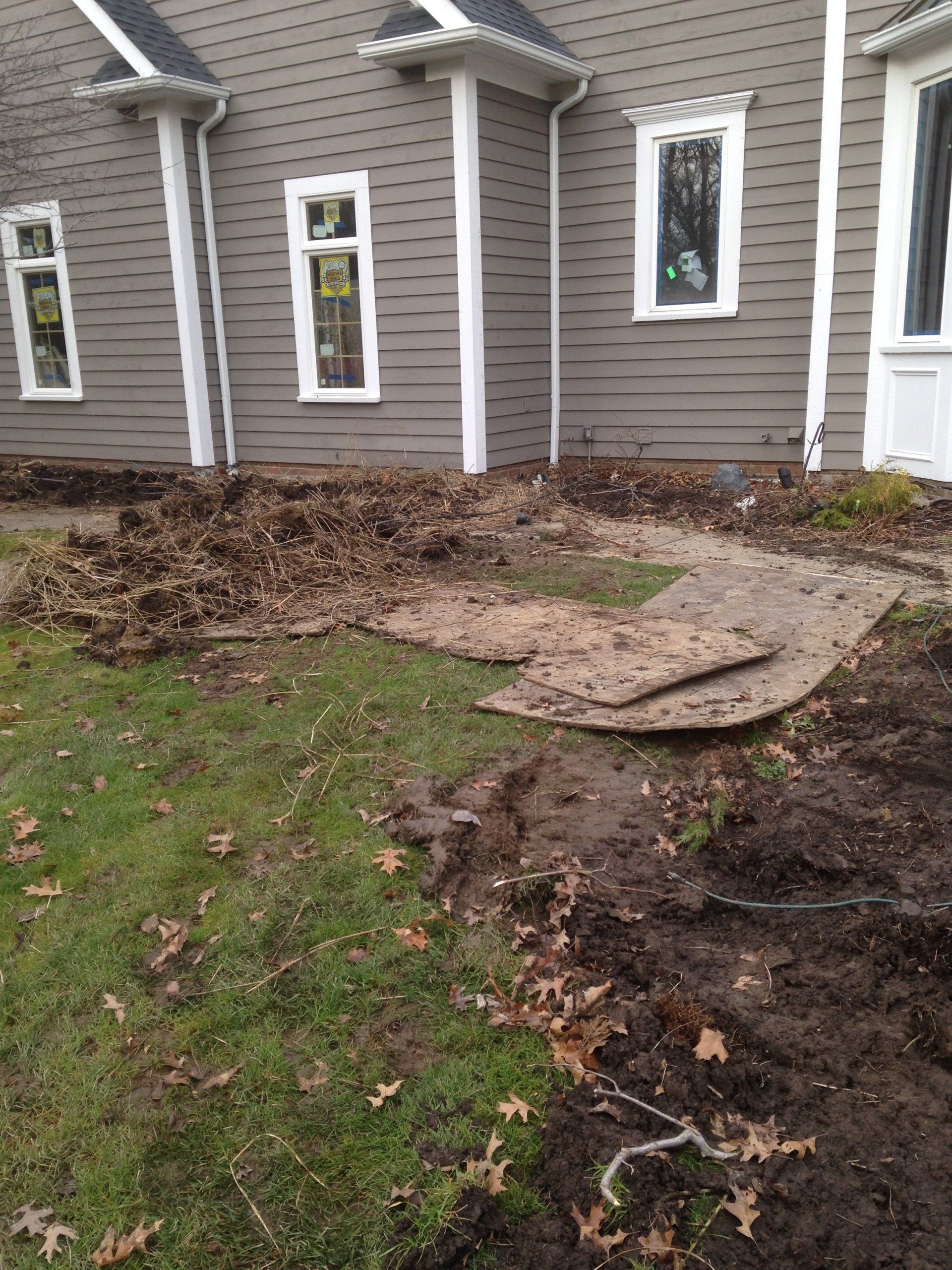 Damaged yard with disturbed soil and broken concrete slabs beside a house exterior