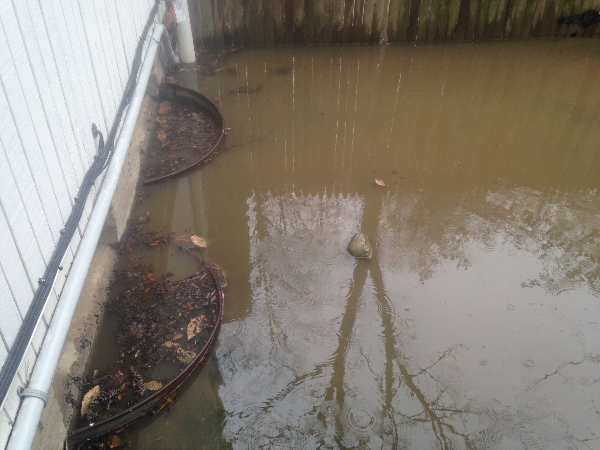 Floodwater beside a white building, with partially submerged round planters along the wall.