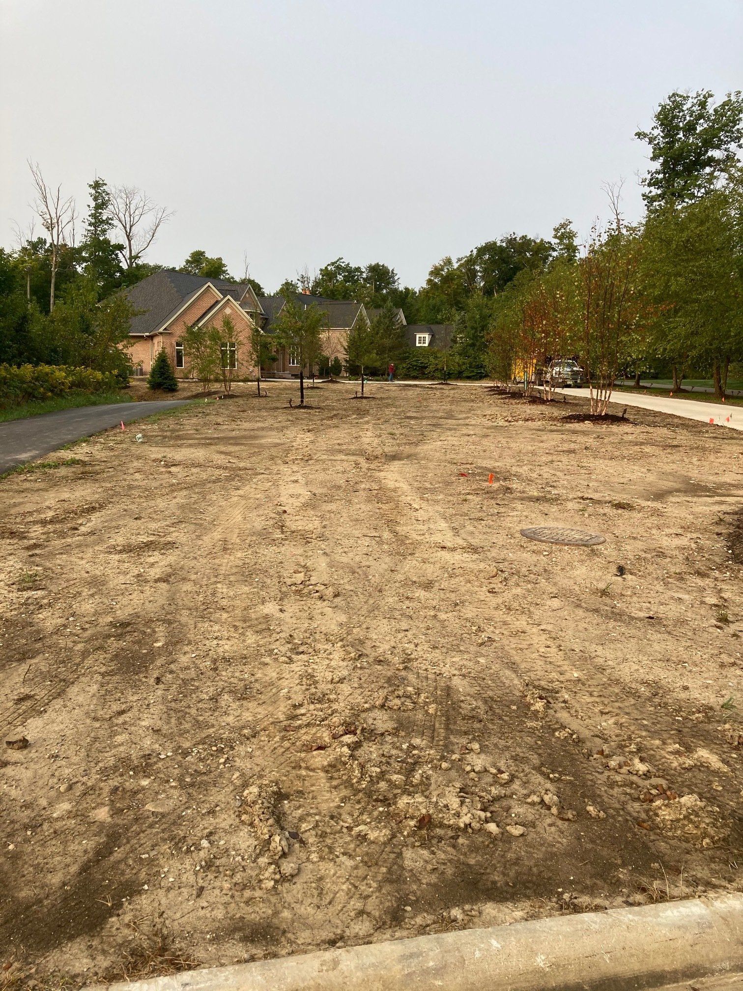 Empty dirt lot in a residential area, with small houses and trees in the background.