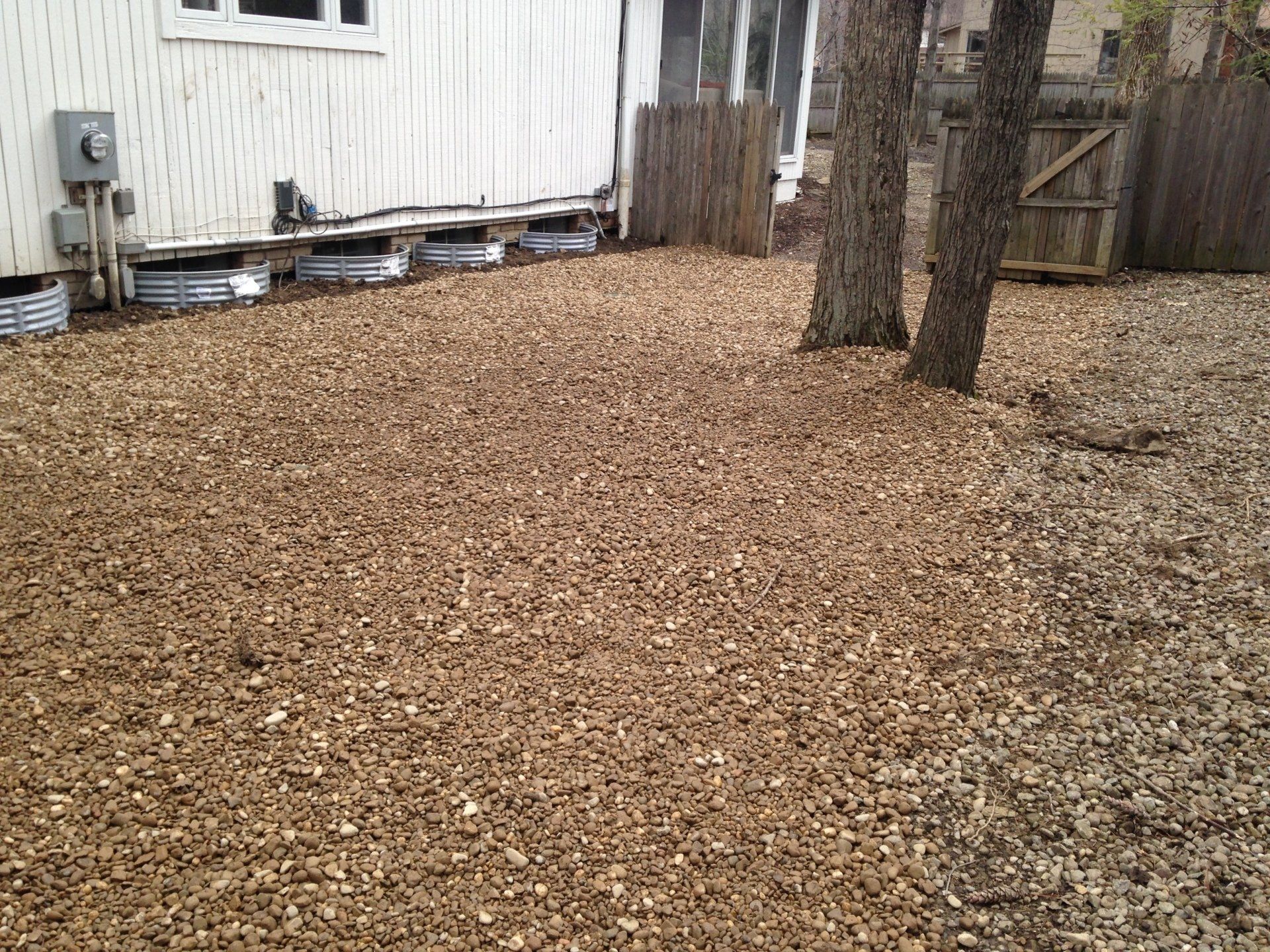 Woodchip-covered yard beside a white house with trees and a wooden fence
