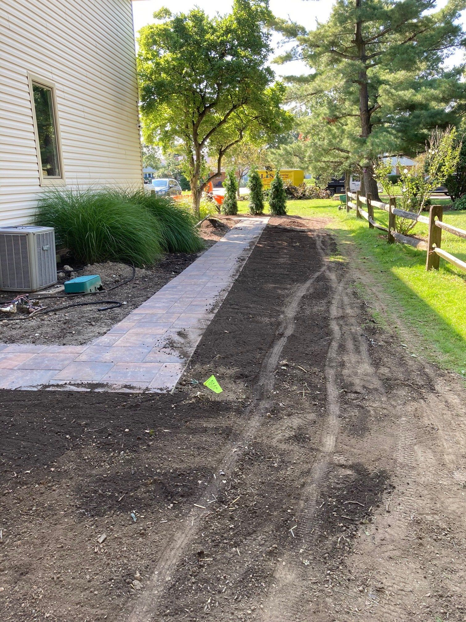 Gravel side yard beside a house, with a stone border, trees, and people working in the distance