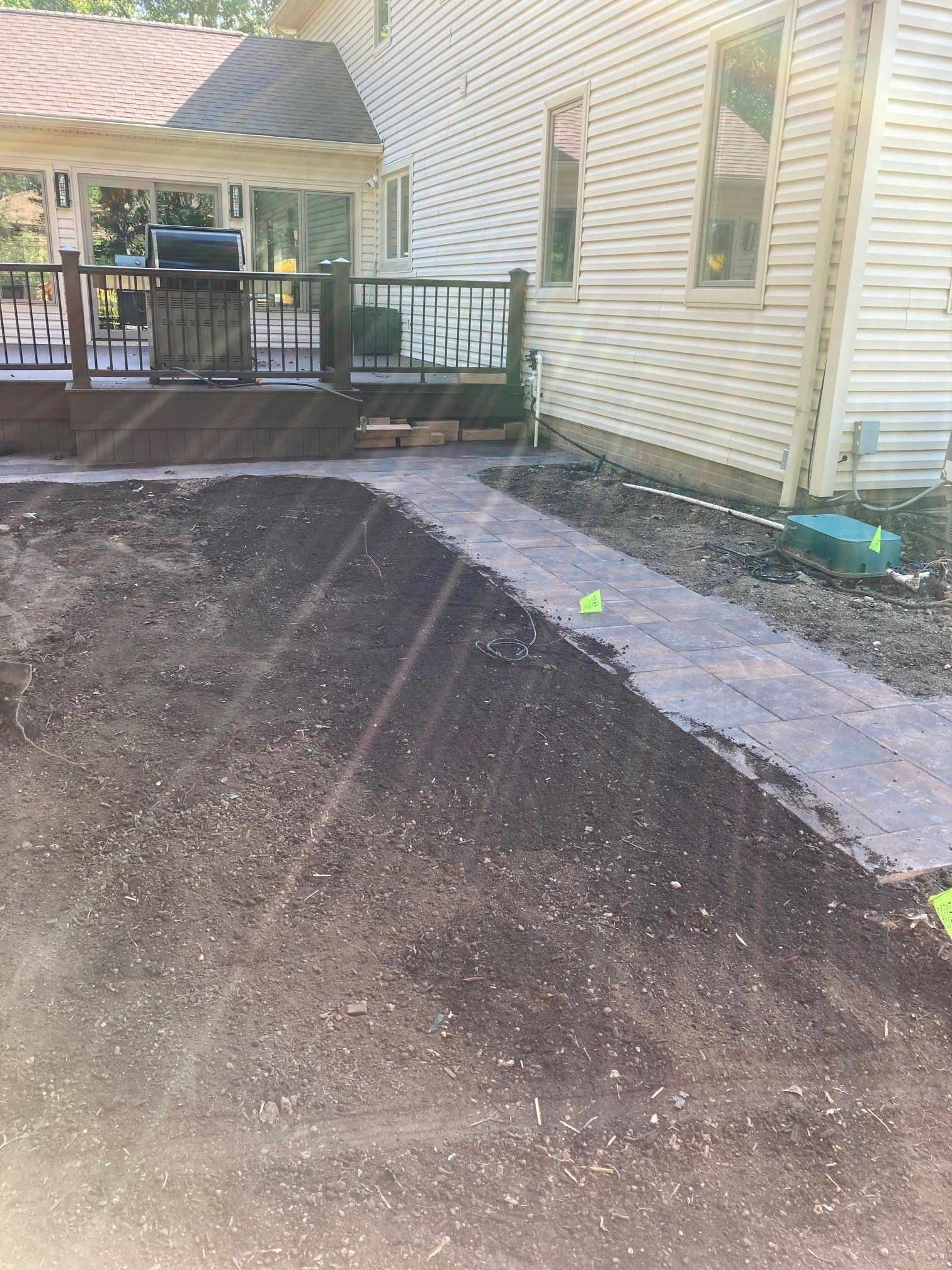Freshly graded dirt beside a house and deck, with a concrete walkway along the side.