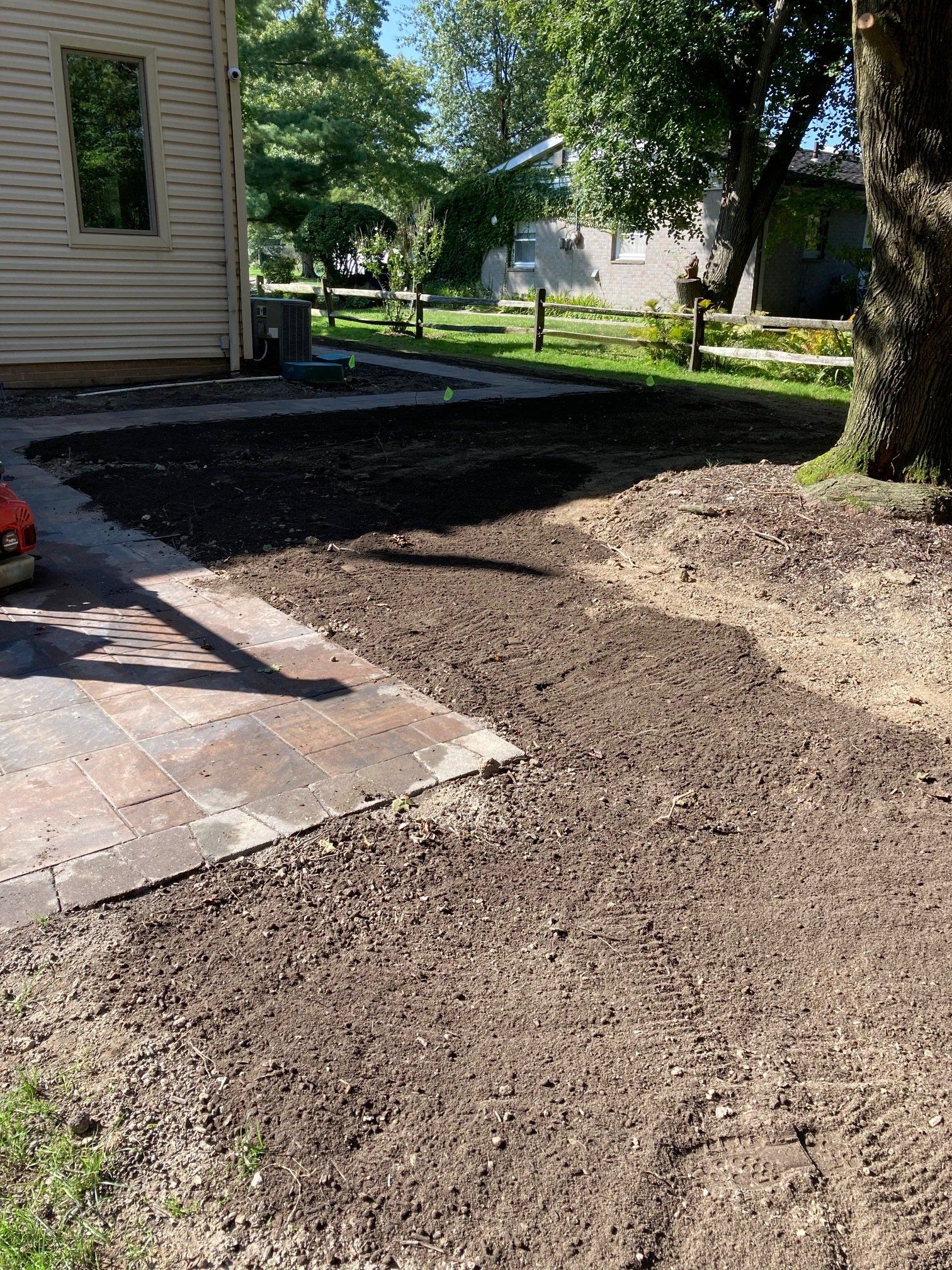 Gravel driveway beside a house, with a tree and sunlit yard in the background.