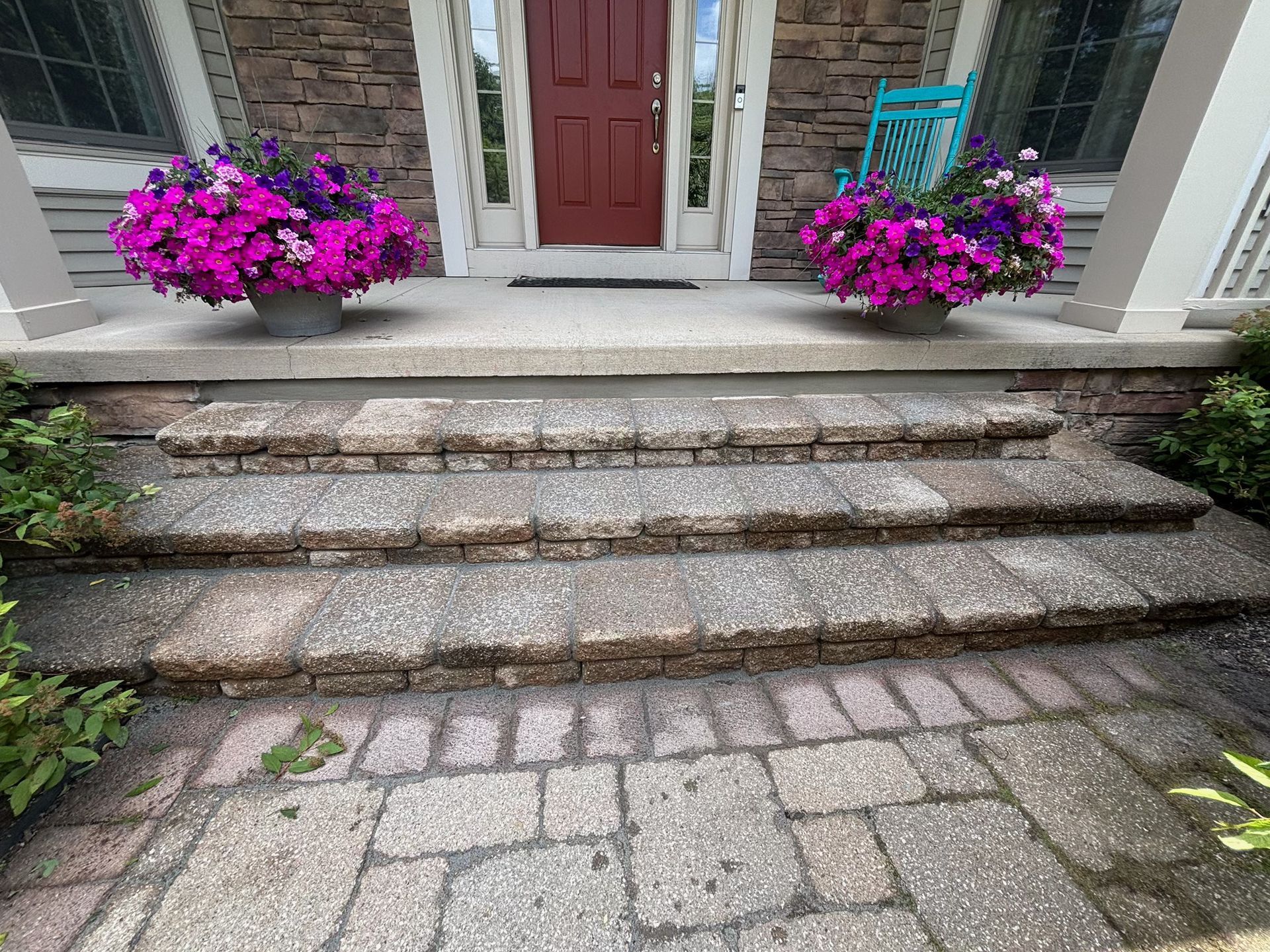 Stone steps leading to a front door, flanked by two bright pink flower planters.