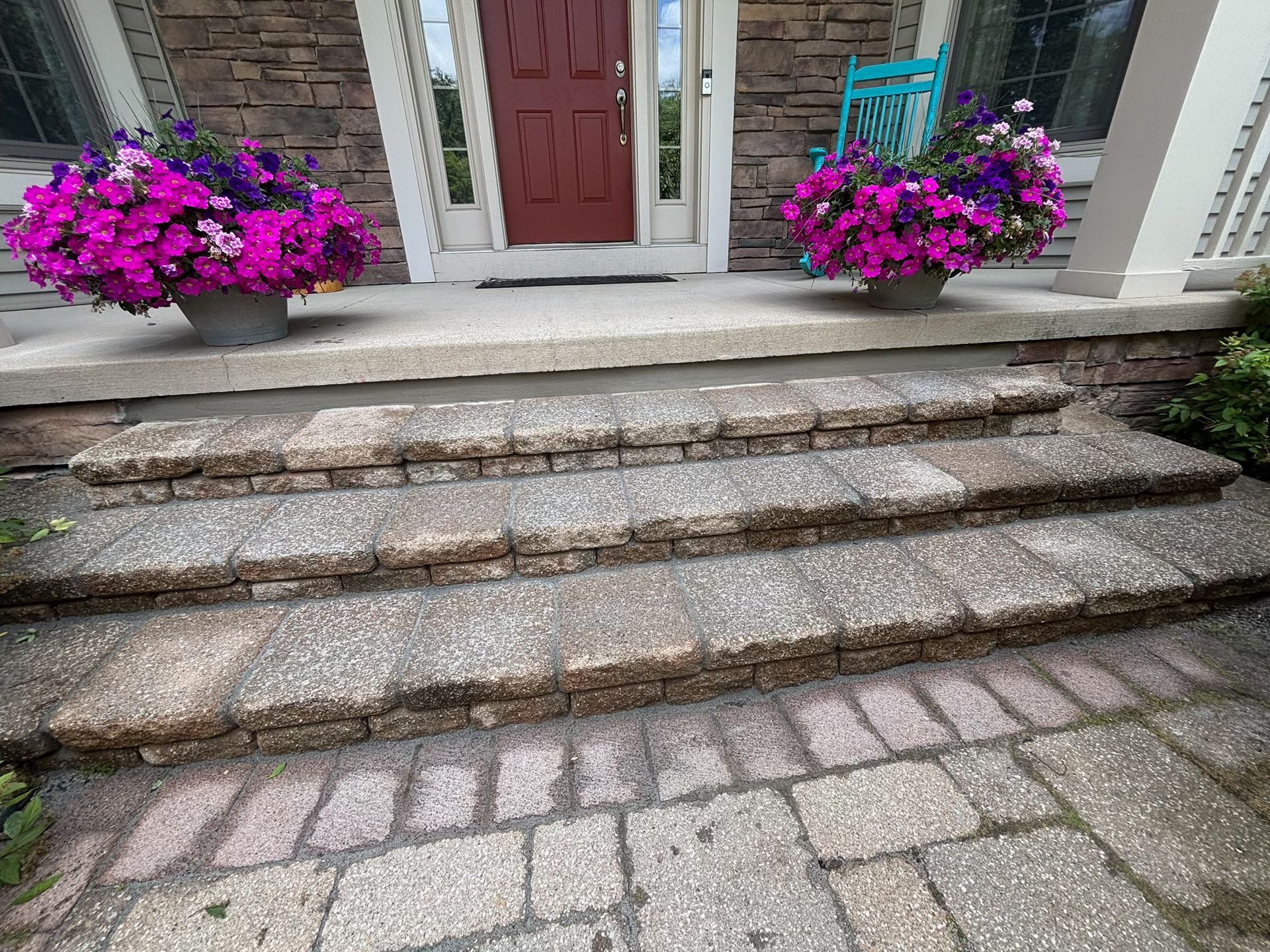 Stone front steps leading to a red door, with pink flowers in planters on both sides