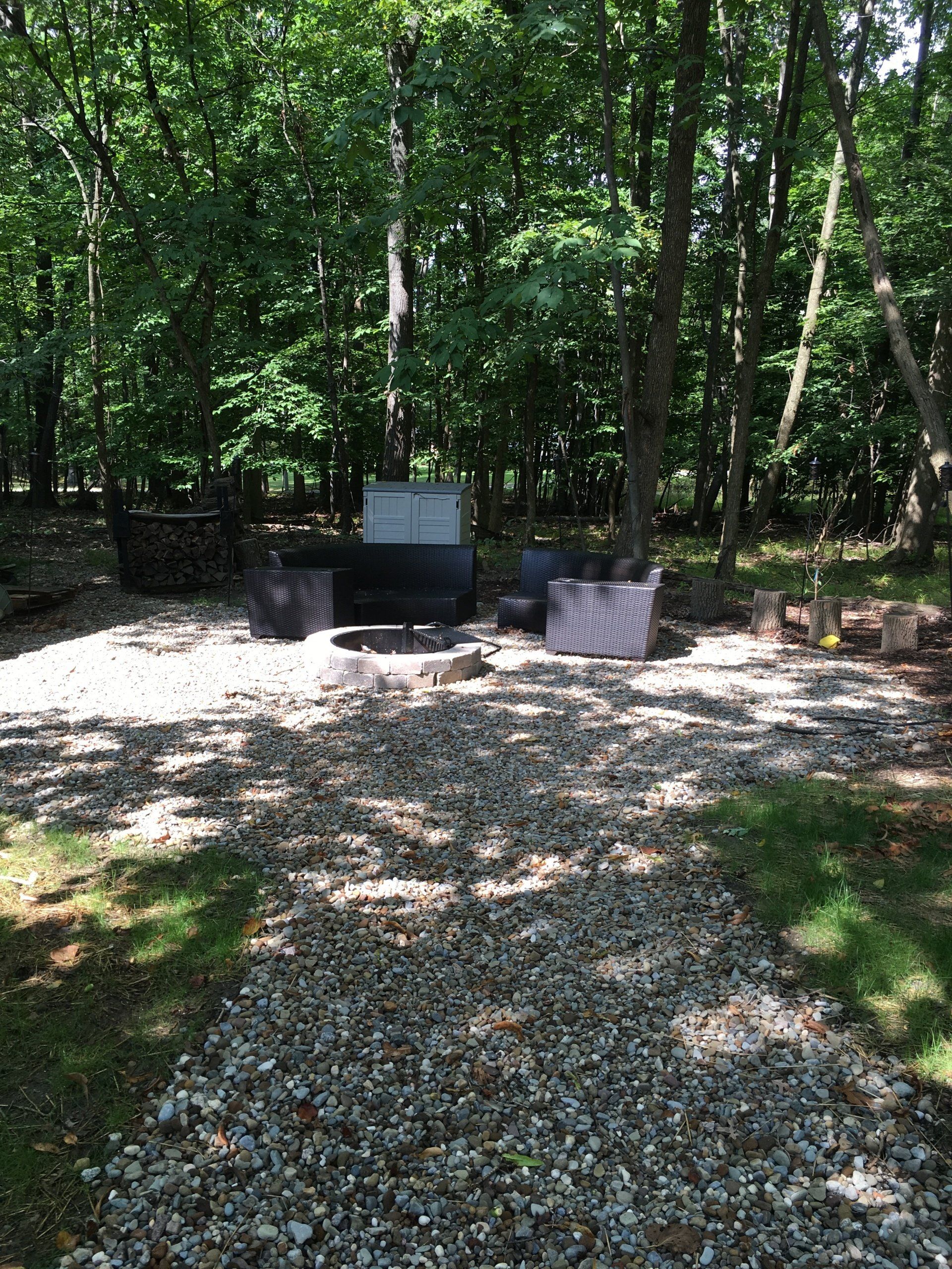 Gravel campsite with fire pit and grills in a wooded area