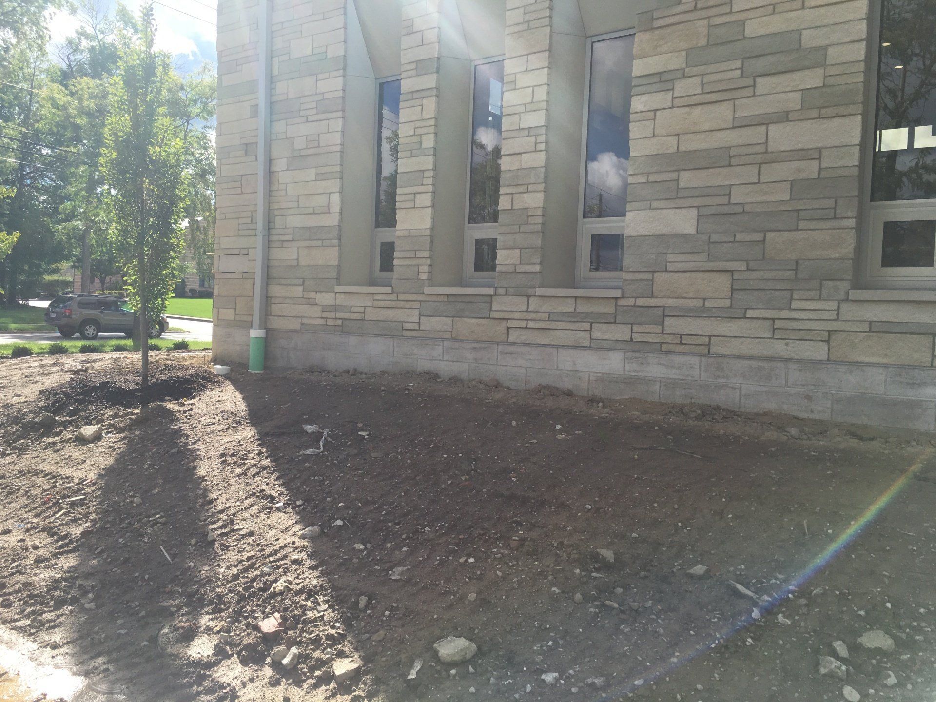 Stone building exterior with narrow windows, dirt landscaping, and sunlight casting long shadows.