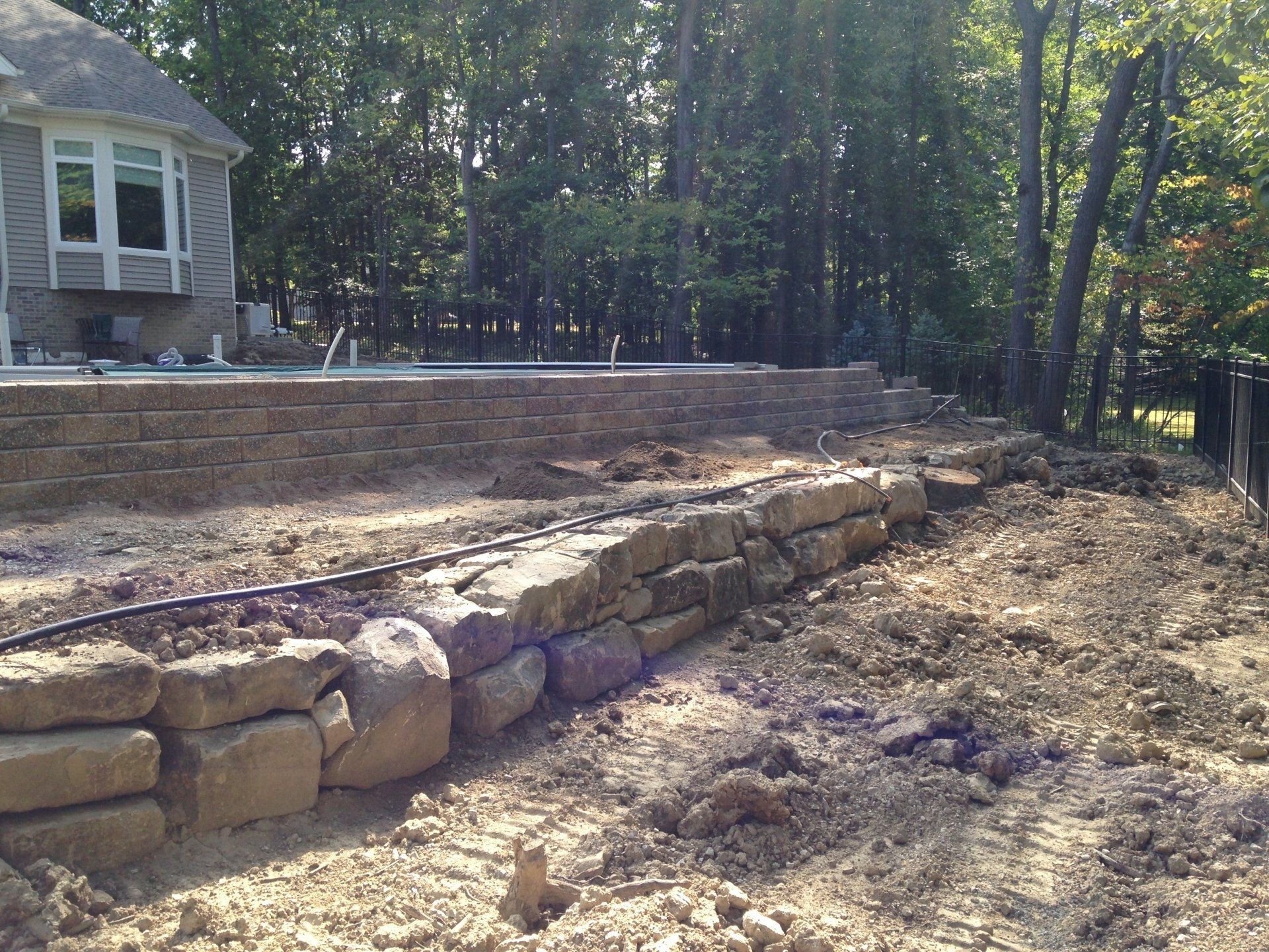 Backyard stone retaining wall and raised patio beside a wooded house