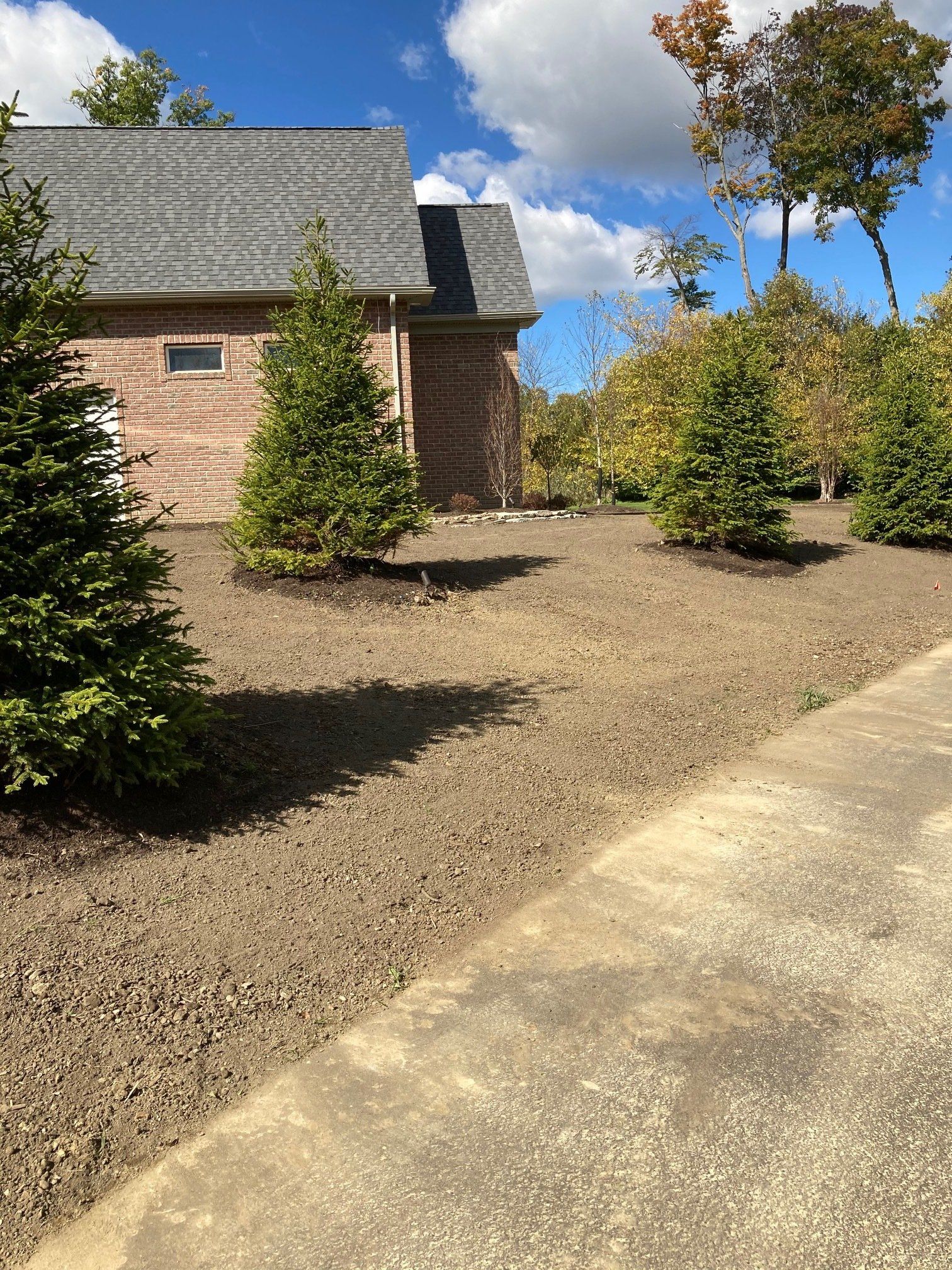 Brick house with gray roof, landscaped shrubs, and a concrete driveway under a blue sky