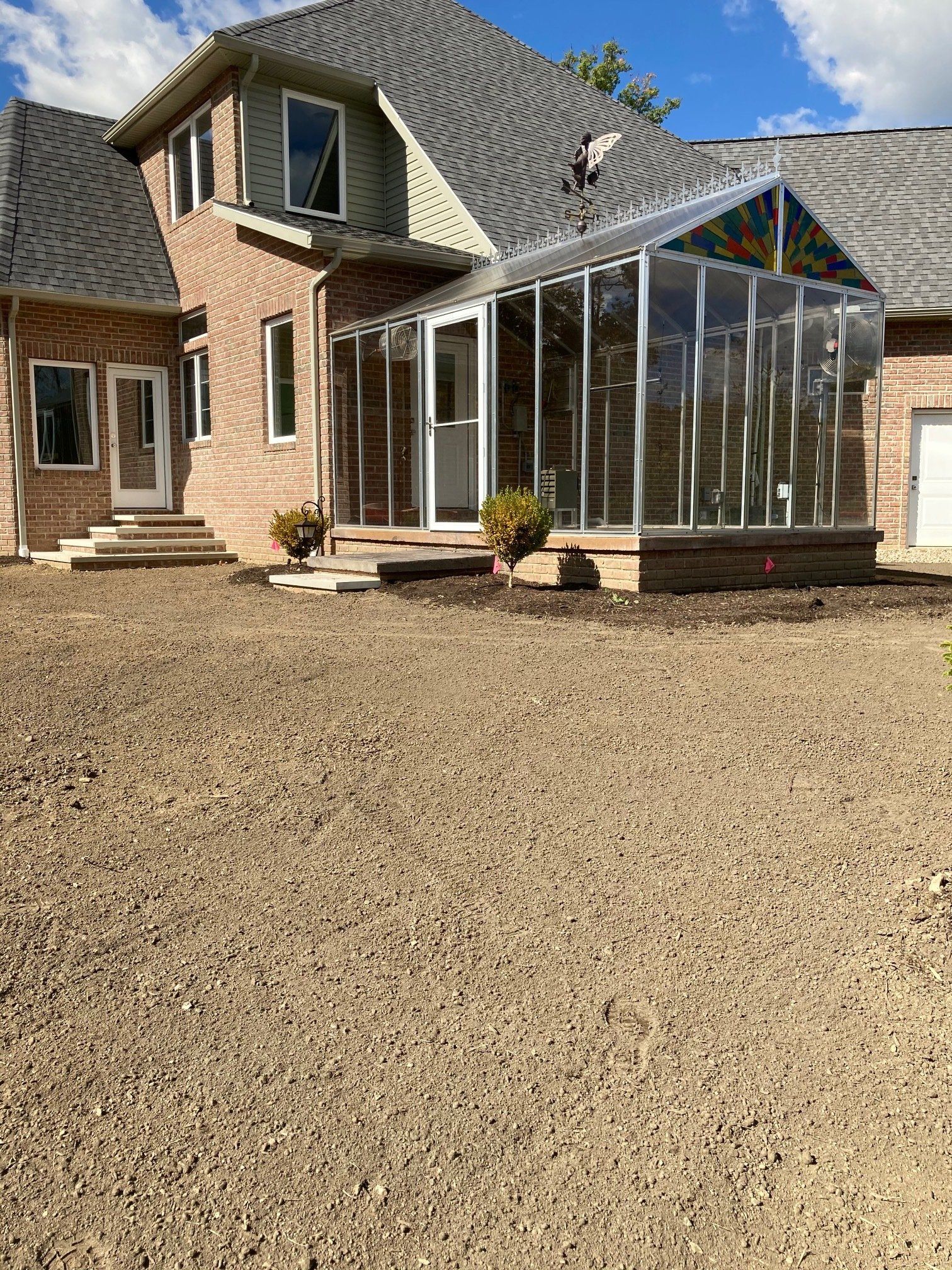 Brick house with a glass sunroom and a large gravel driveway under a blue sky.