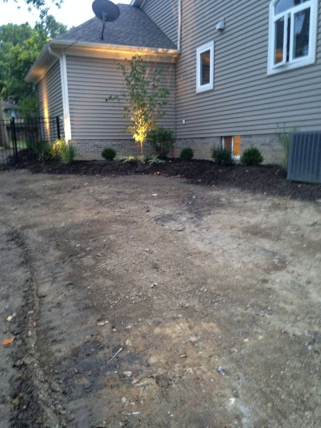 Freshly graded dirt path beside a gray house with small lit shrubs at dusk