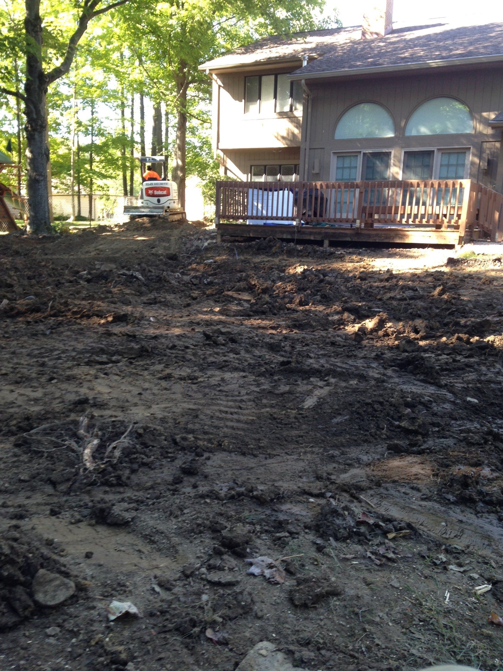 Mud-covered yard beside a house with a wooden porch and parked red truck in the background