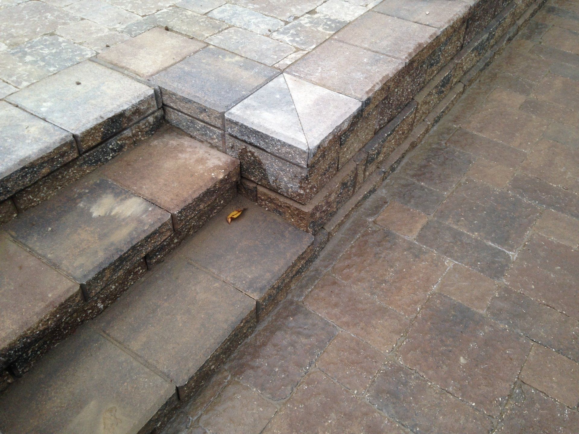 Stone steps beside a paved walkway, with a small curb and weathered brick wall.