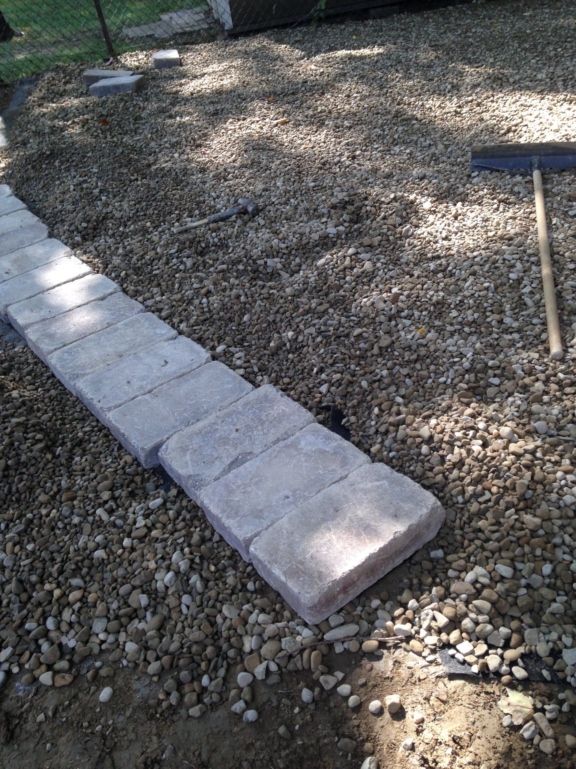 Raised stone border edging a gravel path in a yard, with a small rake nearby.