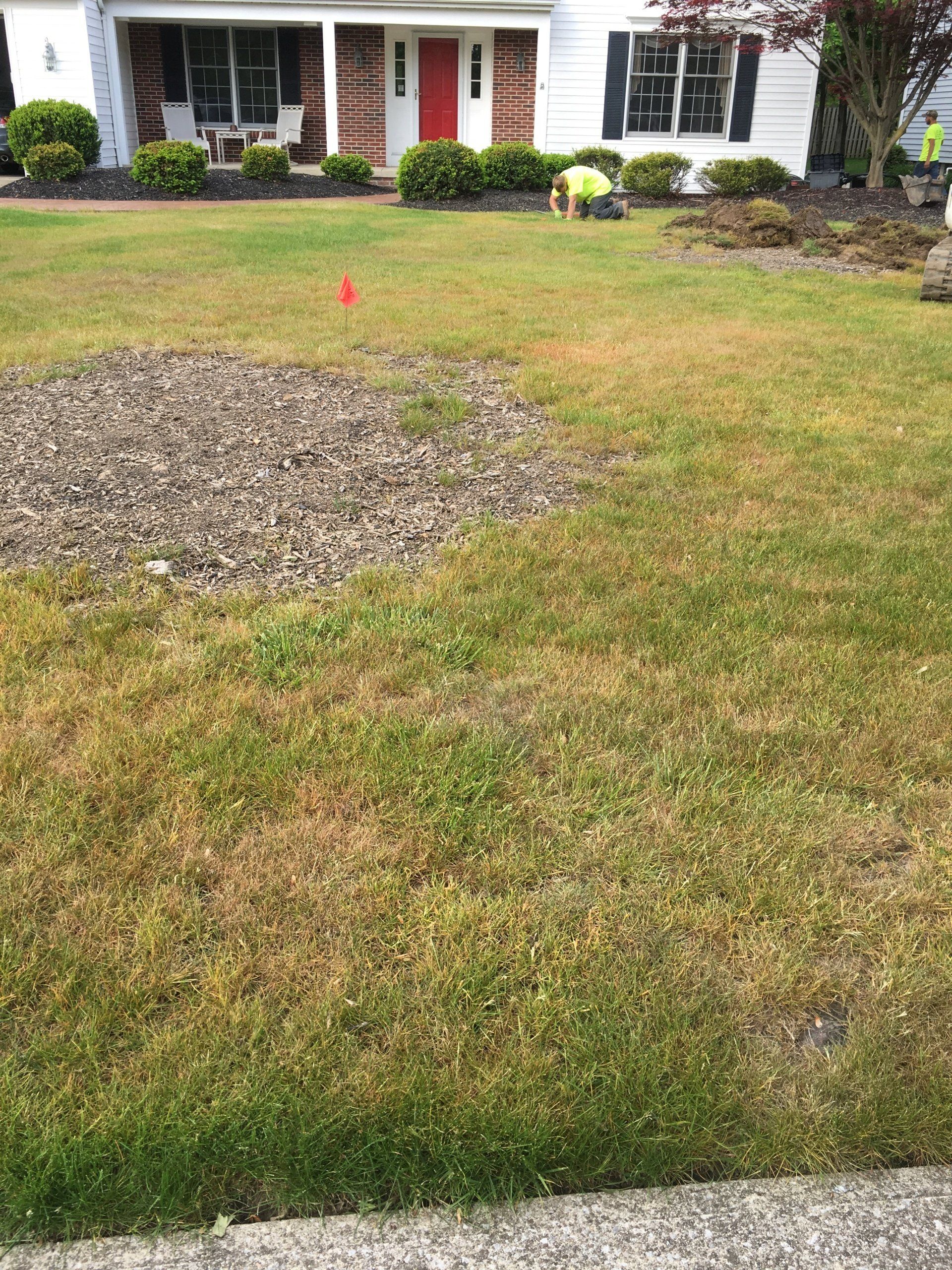 Front yard with a patchy lawn, gravel area, and red marker in front of a white house