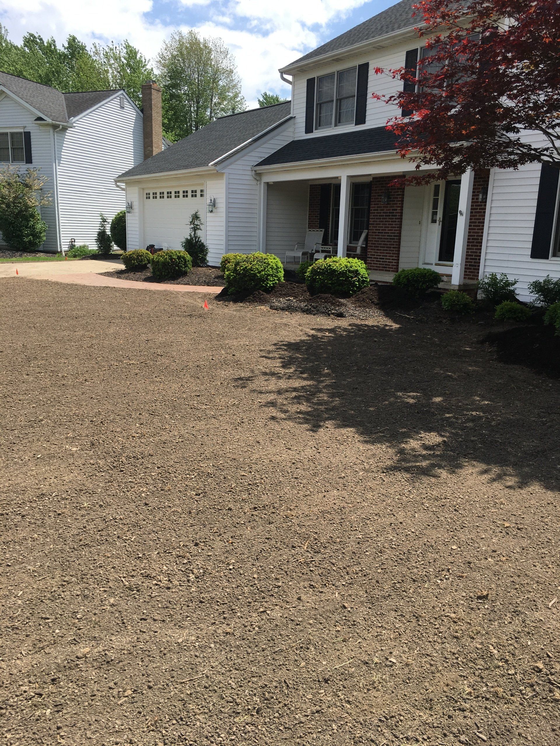 White two-story house with a gravel driveway and a striped awning over the side garage.