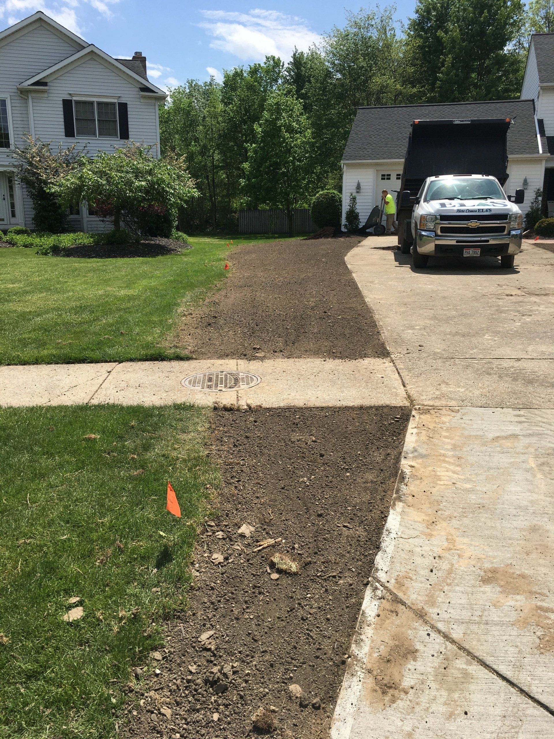 Dirt strip along driveway beside lawn, with a truck parked near a garage in a suburban yard.