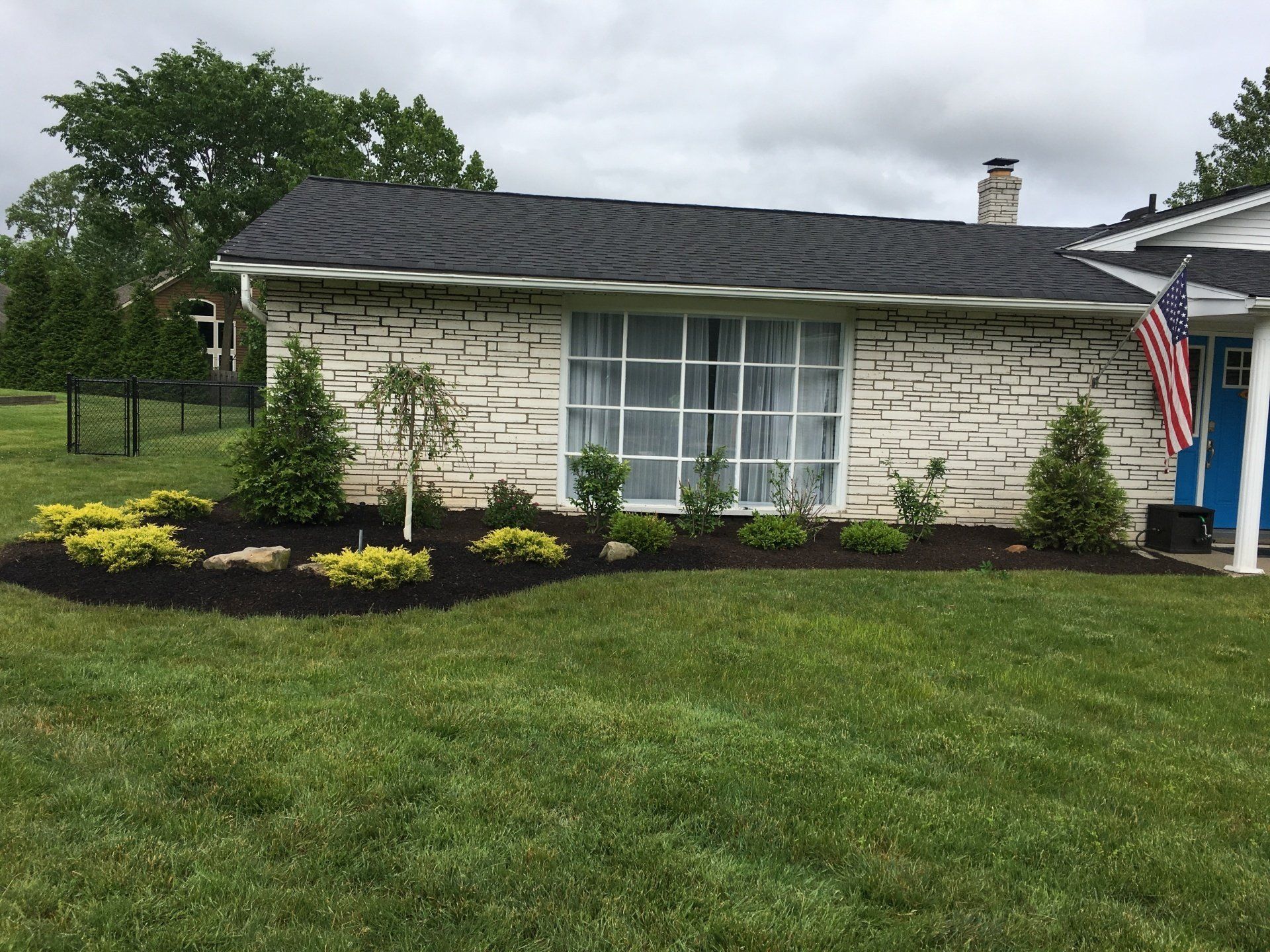 Suburban house with stone facade, large front window, manicured lawn, and American flag by the porch