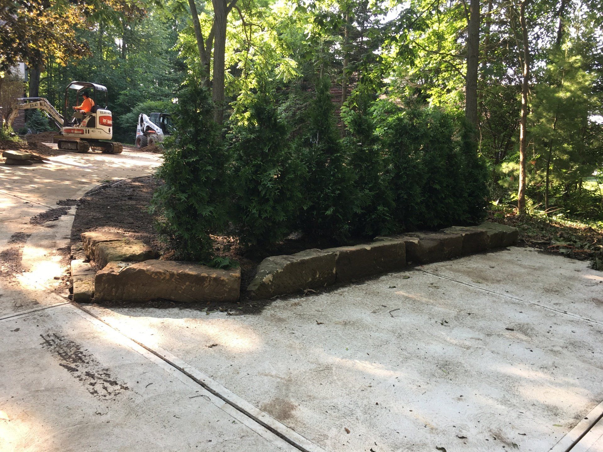 Concrete path through wooded area with stone borders and construction equipment in the background