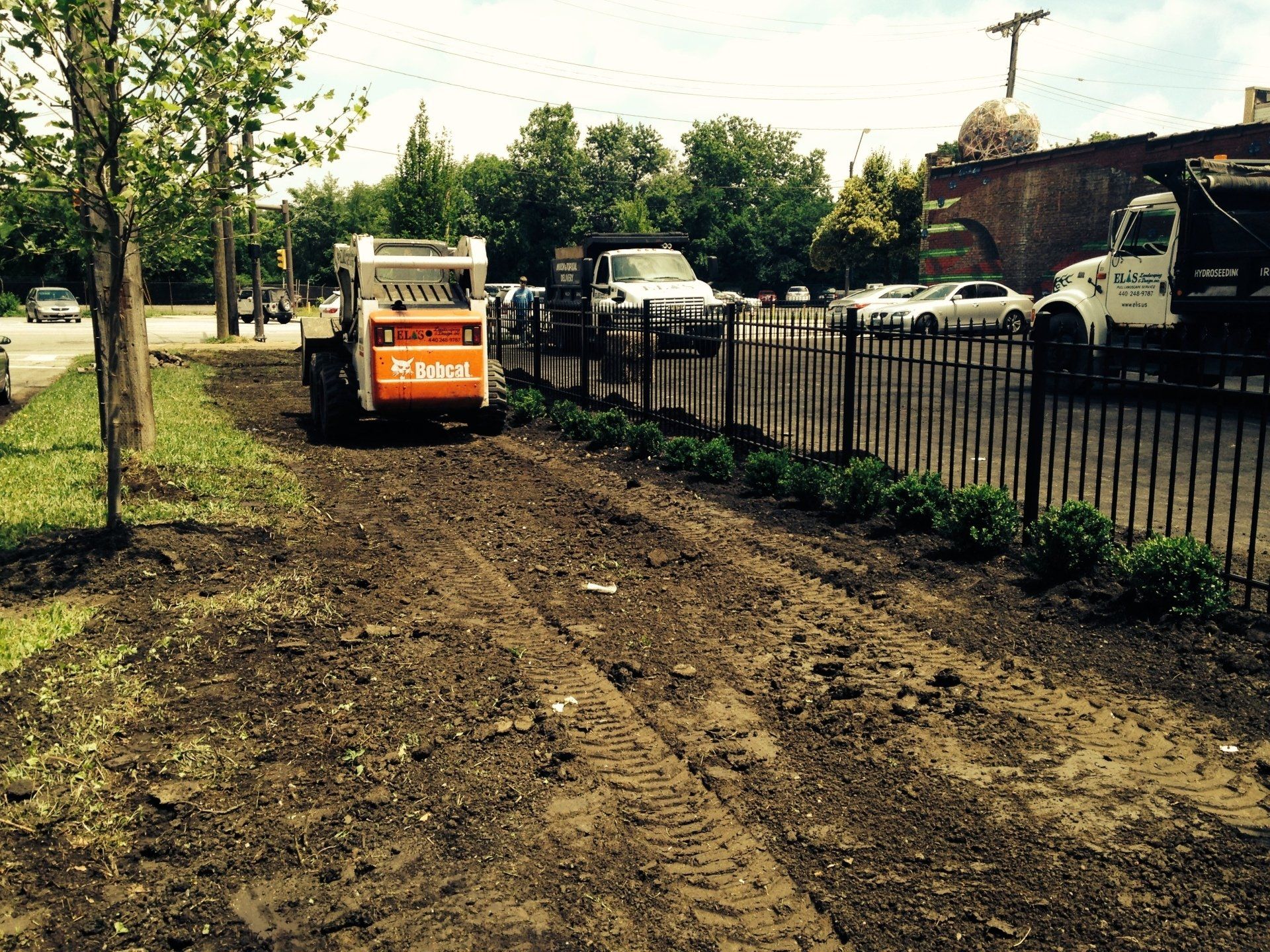 Construction site with orange skid steer clearing dirt beside a street and fence.