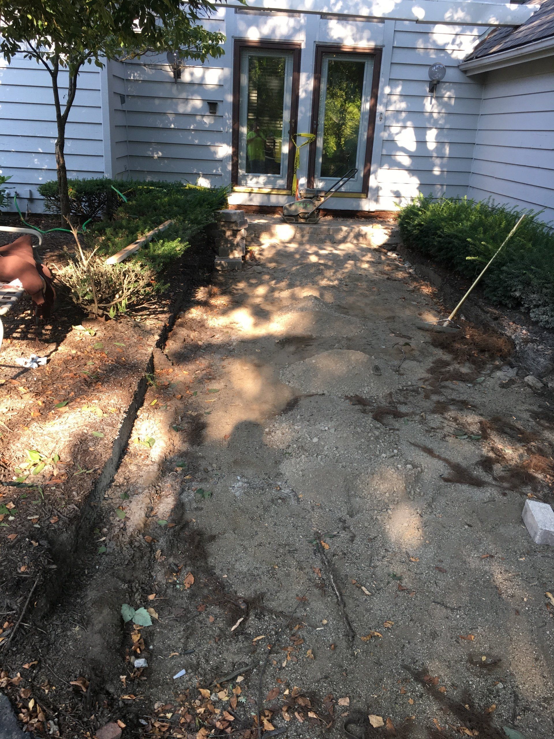 Cracked concrete walkway leading to white double doors beside a house, with garden beds on both sides.