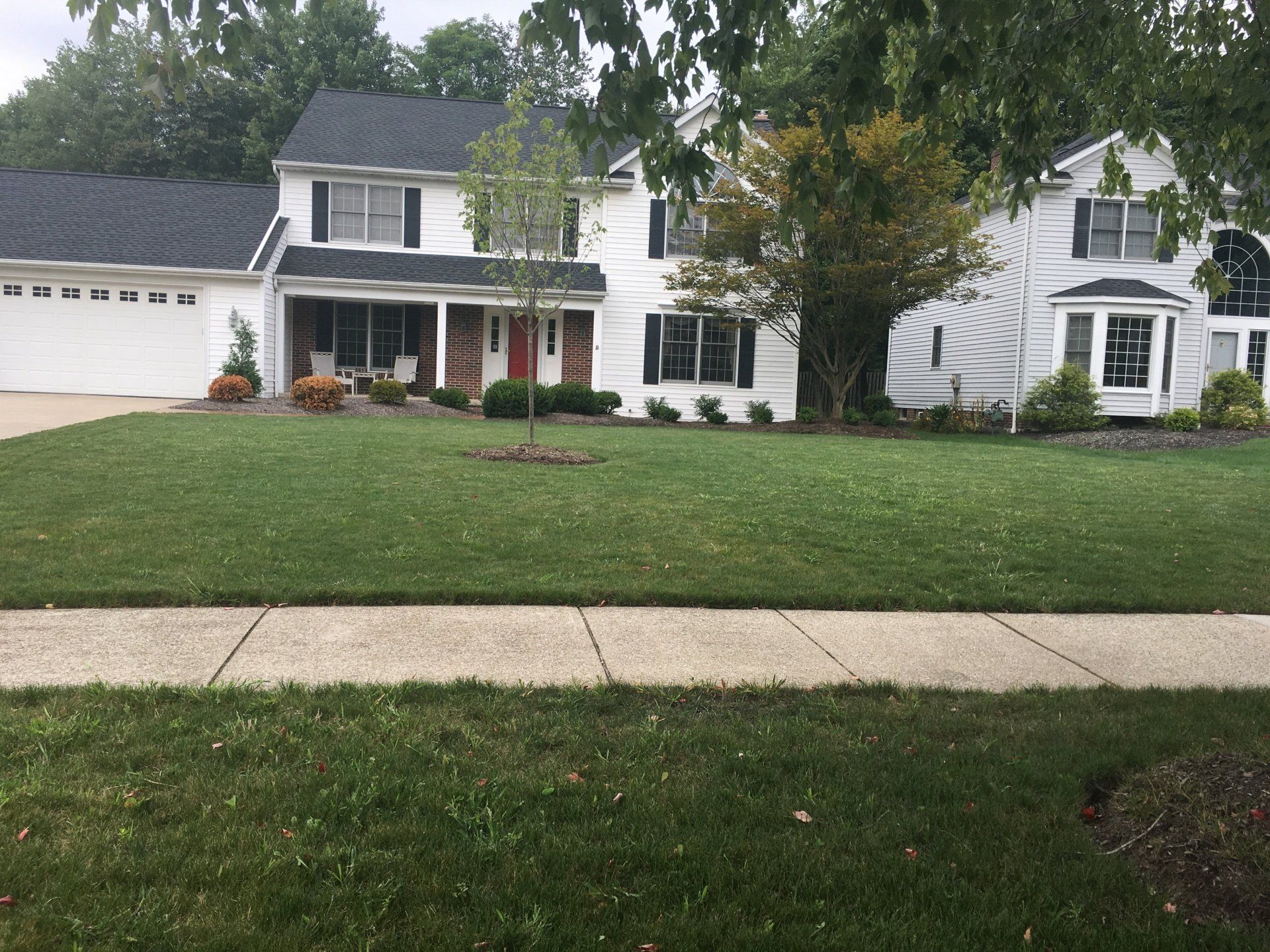 Suburban two-story white house with front porch, garage, and large lawn in front